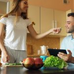 Attractive couple chatting in the kitchen early morning. Beautiful woman feed her husband while cooking breakfast at home